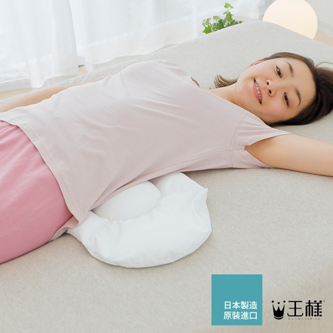 白色腰枕，具有柔軟蓬鬆的填充物，形狀符合人體工學，放置於一位側臥女性的腰部下方，提供支撐。