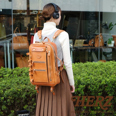 職人手作皮革兩用多功能後背包 R-66，採用光滑棕色皮革製成，設計有頂部提把、兩個前拉鍊口袋、側邊扣帶和可調節肩帶，適合日常使用。