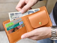 職人手作的經典雙折短夾，採用天然棕色皮革製成，有掀蓋與銅扣設計，內含多個卡槽，其中一個卡槽放入了日圓千元鈔票，另有信用卡與VISA卡。