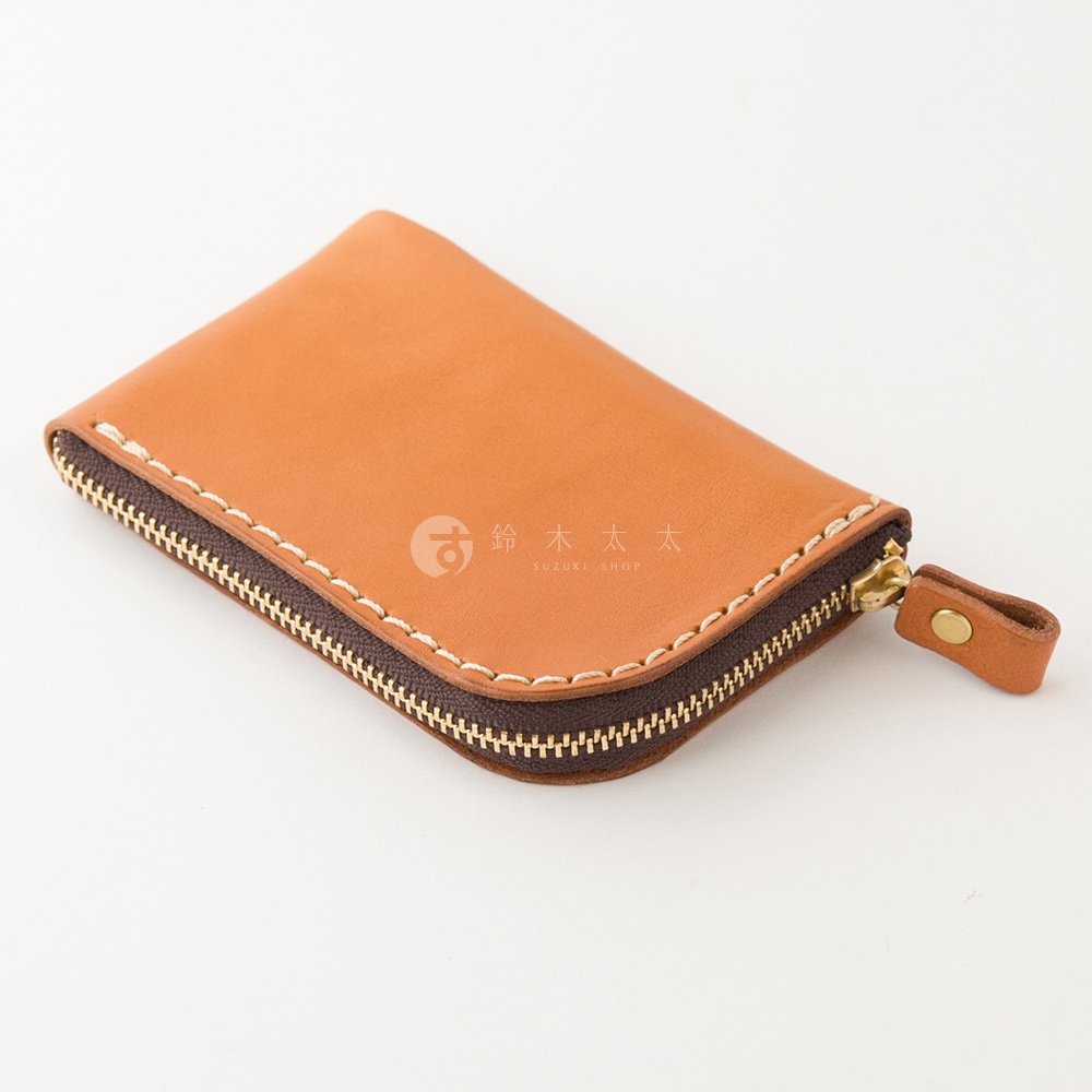一個以斜角視角呈現的日本HERZ職人手作迷你皮夾，採用淺棕色Stare皮革製成，表面有細緻的手工縫線與深褐色拉鍊設計，拉鍊末端附有同色皮革拉環與金屬扣飾，整體外觀簡約精緻。