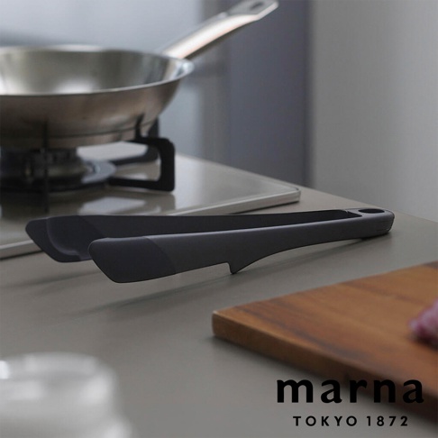 marna TOKYO 1872 標誌旁為一組灰色食物夾，後方為廚房爐具上的不鏽鋼鍋。