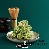 一堆抹茶杏仁卷，外層裹滿翠綠色杏仁碎，內部為淡黃色，堆疊在淺灰色盤子上，背景為深綠色。右側有日本茶筅和黑色茶罐。