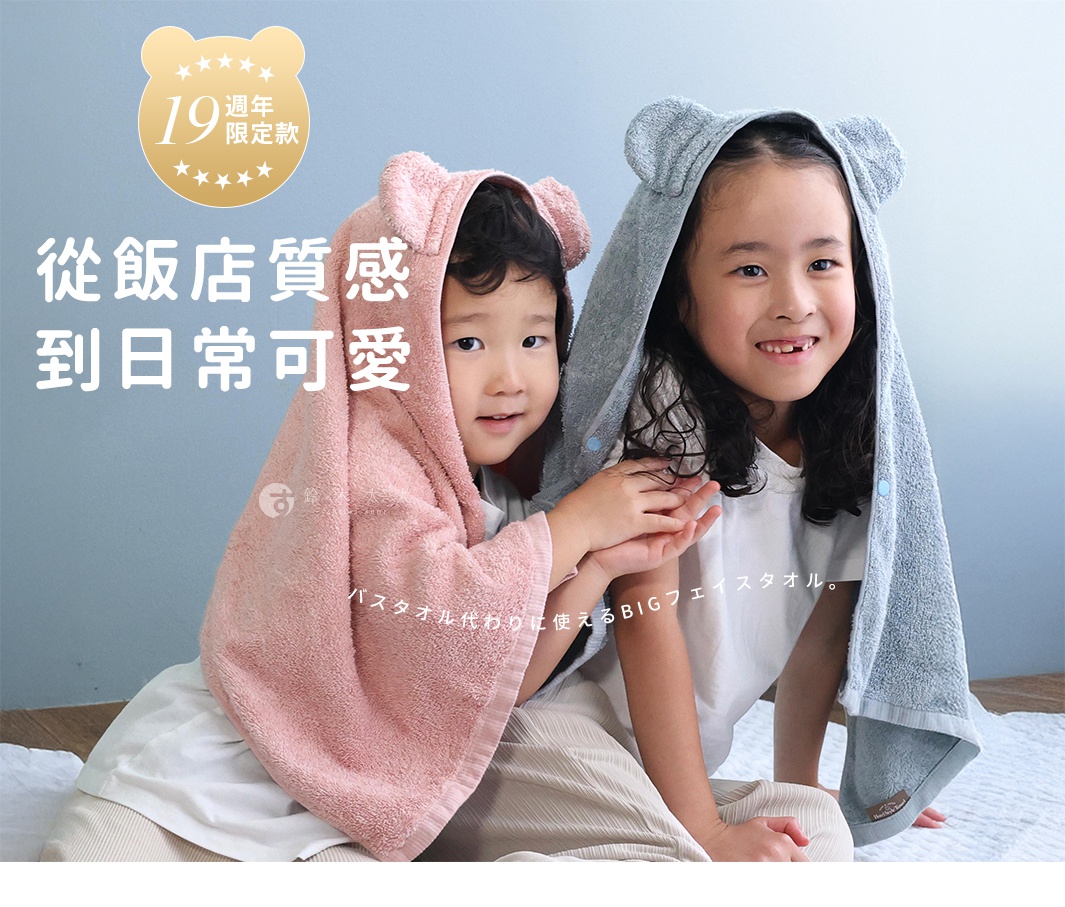 兩位小朋友穿著可愛的熊耳造型連帽毛巾，一位披著粉紅色毛巾，另一位披著灰色毛巾，背景為淺藍色牆壁。
