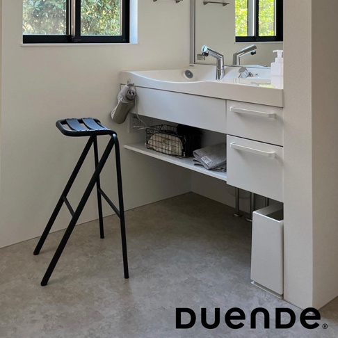 黑色金屬框架的吧檯椅，椅面為黑色皮革，椅腿呈A字型結構，椅面設計成可折疊的造型，適合放置於衛浴空間。