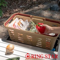 卡其色塑膠長型購物籃，裝有蔬菜、肉類和包裝食品。籃子有兩個紅色提把，側邊有長方形簍空設計。一只手正將一顆紅甜椒放入籃中。