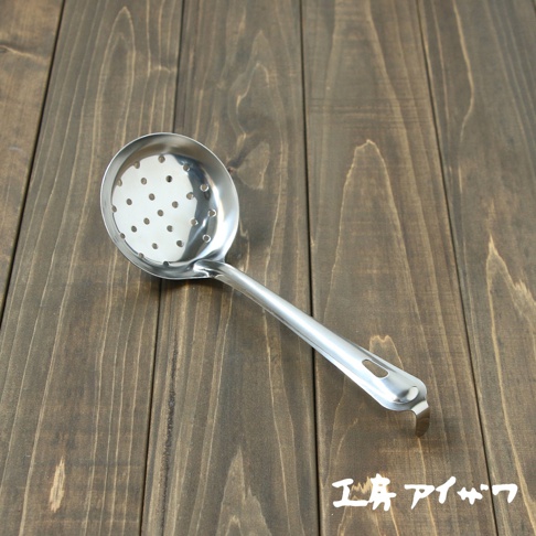 一個帶有圓形孔洞的不鏽鋼中型撈勺，勺面為銀色金屬光澤，勺柄末端有掛孔及彎鉤，放置於深棕色木紋背景上。