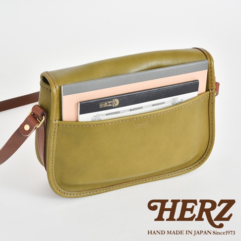 橄欖綠皮革職人手作傳統釣魚包，設有前方置物袋，可放入筆記本，搭配棕色皮革背帶，包身線條簡潔。