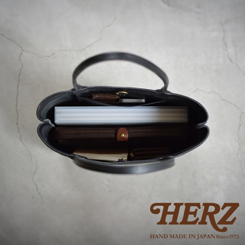 HERZ HAND MADE IN JAPAN Since1973，黑色皮革托特包內部，可見文件夾、筆記本、手機及零錢包。