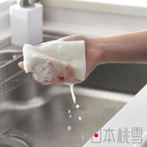 一隻手正拿著含有泡沫的白色洗碗海綿，水從海綿滴落至水槽中，右下方有「日本桃雪」的標誌。