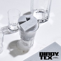 灰色耐用海綿刷置於充滿泡沫的玻璃杯內，旁邊還有其他透明玻璃杯，整體佈局乾淨明亮。