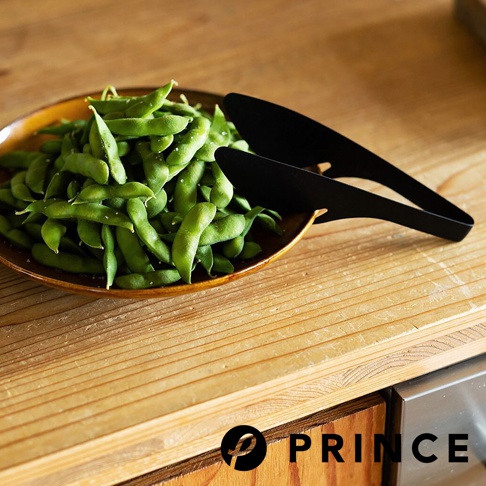 黑色萬用料理勺型分菜夾，夾著一盤裝有鹽粒的毛豆，放在木製桌面上。