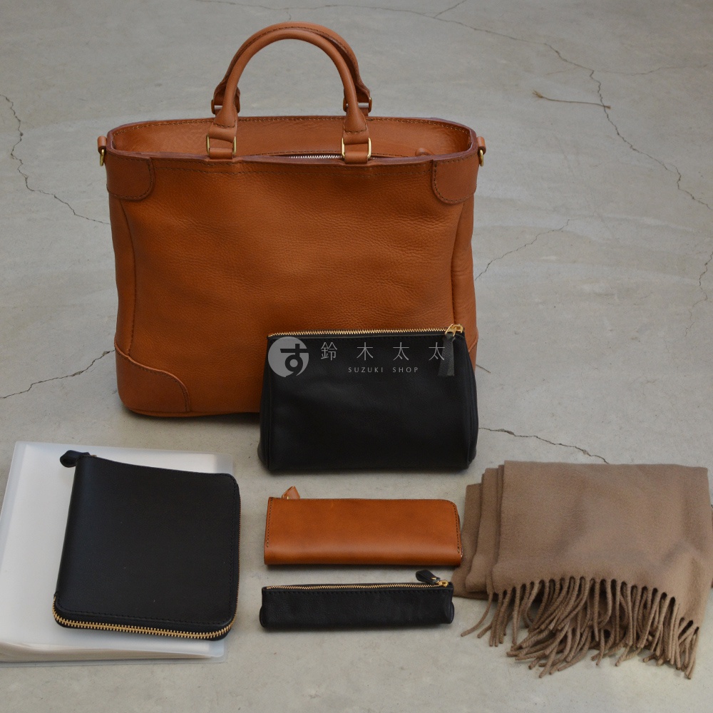 職人手作皮革Organ兩用商務托特包，主體為棕褐色荔枝紋皮革，搭配金色拉鍊。包內含一個黑色皮革拉鍊小包、一個棕褐色皮革長夾、一個黑色皮革筆袋，以及一個透明文件夾和一條米色羊絨圍巾。
