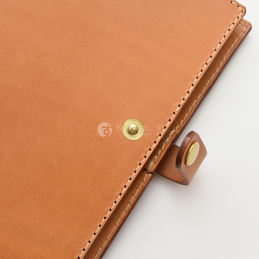 職人手作皮革A5手帳/記事本書套，為淺棕色皮革材質，配有黃銅色圓形按扣和皮革束帶。