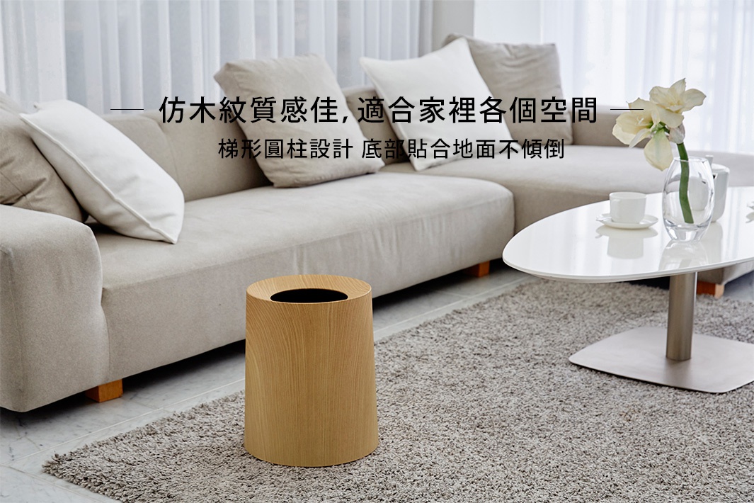 橡木紋路圓柱形垃圾桶，木質紋理呈現自然的暖色調，開口處為黑色內襯，置於灰色地毯上，背景為淺色沙發。