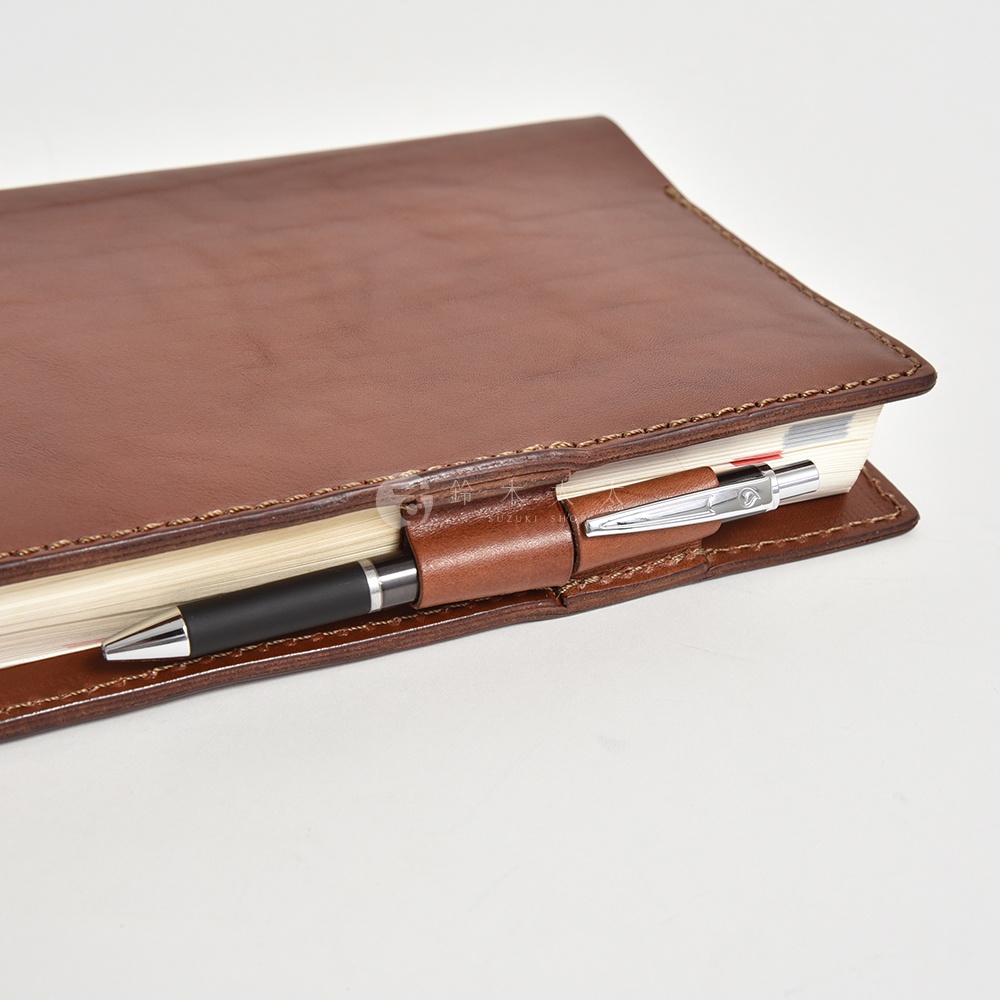 棕色皮革手帳書套，內有筆夾固定一支黑色筆，書套邊緣縫線清晰，特寫鏡頭。