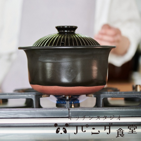 Kitchen Studio Panda食堂 萬古燒職人炊飯土鍋，黑色陶鍋放在瓦斯爐上烹煮，上方有竹編蒸籠式的鍋蓋。