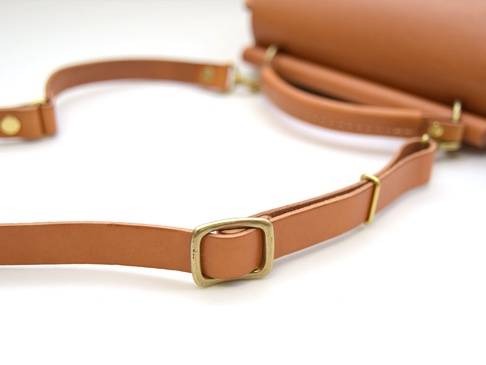 棕色皮革製成的兩用單肩包，配有可調節的肩帶和黃銅色金屬扣環。