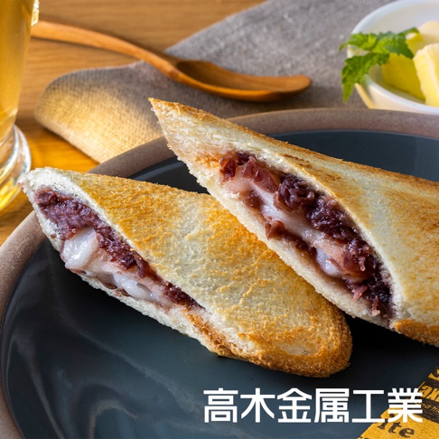 兩片烤過的吐司夾著紅豆餡和麻糬，呈現金黃色澤，擺放在深灰色盤子上，背景有木勺和一杯飲品。