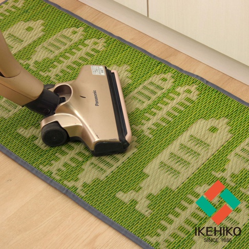 綠色藺草編織的長方形廚房地墊，織紋中帶有淺色圖案，邊緣為深灰色滾邊，一臺金屬色吸塵器頭正放在地墊上。