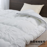 一床蓬鬆的白色羽絨被，帶有深藍色滾邊，置於床上，背景是深色木製床頭板和一個奶油色枕頭。