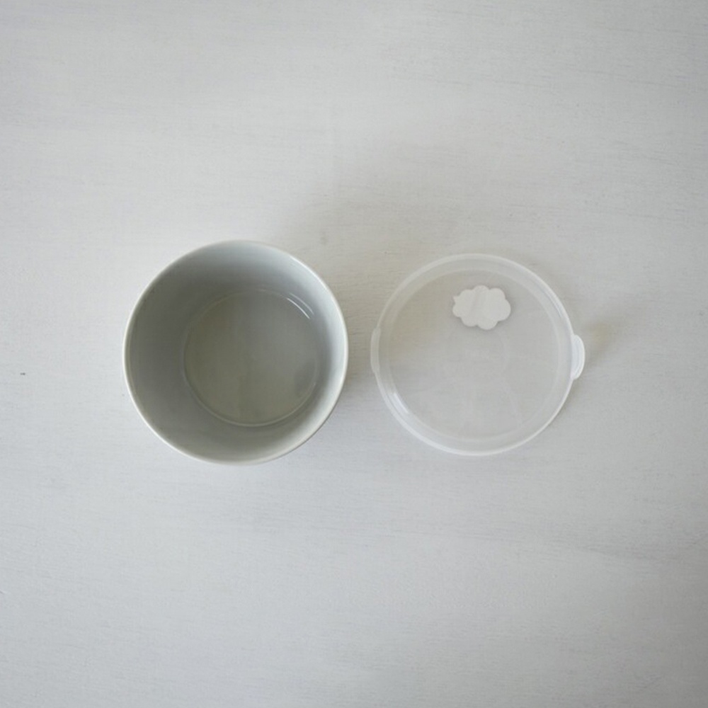 一個灰色的陶瓷碗，旁邊有一個透明的白色塑膠蓋，蓋子上有一個淺色的雲朵圖案。