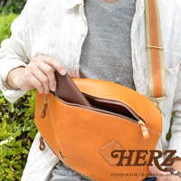 橘色皮革製成的職人手作多功能收納斜背包，包身圓潤，配有可調節的帆布與皮革拼接斜背帶，並露出部分內側的棕色皮革長夾。