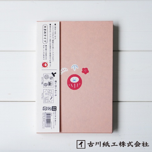粉色美濃和紙製成的御朱印帳，封面中央印有紅色達摩吉祥物圖案，搭配一朵小紅花和藍色箭頭圖案。左側紙帶印有日文說明及多個印章圖案。