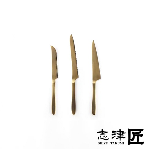 三把金色金屬麵包刀，刀刃分別為鋸齒狀、波浪狀鋸齒狀及平滑狀，置於白色背景上。
