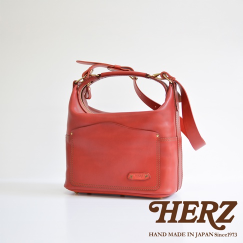 紅色厚實皮革單肩波士頓包，配有拉鍊開合、前袋、側袋及可調節肩帶，黃銅五金配件，手工縫製。