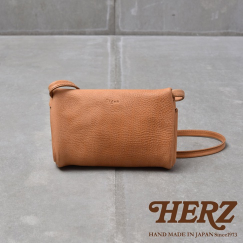 皮革材質的棕色斜背包，表面有細緻紋理，包身上方壓印有 Organ 字樣，下方則有 HERZ 品牌標誌與 HAND MADE IN JAPAN Since1973 字樣
