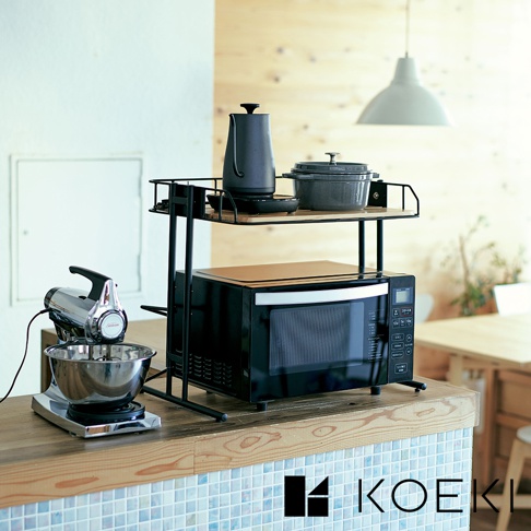 黑色金屬材質的單層桌面收納架，架上擺放著黑色手沖壺與灰色鑄鐵鍋，下方為黑色微波爐，微波爐上方覆蓋木質隔熱墊，左側有銀色手持攪拌機與不鏽鋼攪拌盆。