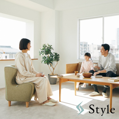 綠色布藝單人沙發，造型獨特，扶手延伸至椅背，坐著一位身穿米色連帽衫的女士，手持杯子。