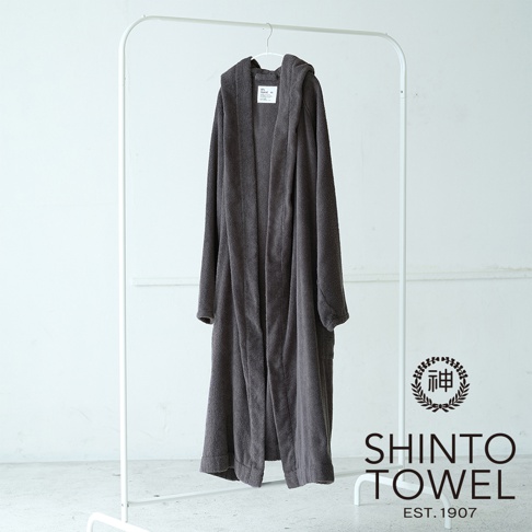 一件深灰色連帽浴袍，材質蓬厚，垂掛在白色衣架上，左側為產品標籤，右下角有SHINTO TOWEL EST. 1907標誌。