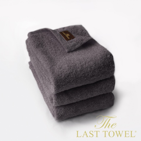 The LAST TOWEL 魔法瞬吸純棉柔毛巾三入組，展示的是三條疊放的深灰色純棉毛巾，質地柔軟蓬鬆，其中一條毛巾的邊緣有品牌標籤。