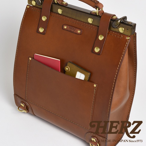 職人手作皮革復古口金後背包 P-7，以棕色皮革製成，設有前置貼袋，可放入護照與卡片，搭配黃銅色金屬口金與鉚釘，展現經典工藝。