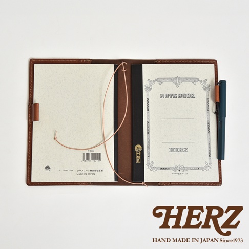 皮革手帳書套打開，內頁一側有筆記本，另一側為空白內頁，書套旁插有深綠色鋼筆。