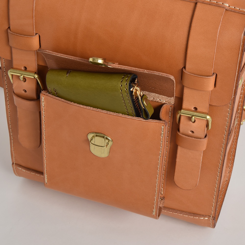職人手作皮革經典學院風後背包 R-100 駝色款，特寫顯示其外部皮革質感、金屬扣環與綠色皮夾。