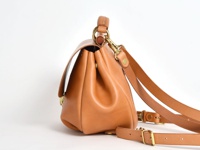 職人手作皮革屋瓦風迷你後背包，採用天然棕色皮革製成，帶有復古金色金屬扣環和可調節肩帶。包身側面呈現圓潤的線條，頂部提把設計。