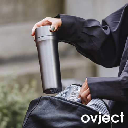 一只手正將一個銀色金屬材質、直筒造型的三用保溫瓶放入一個黑色皮質包中。