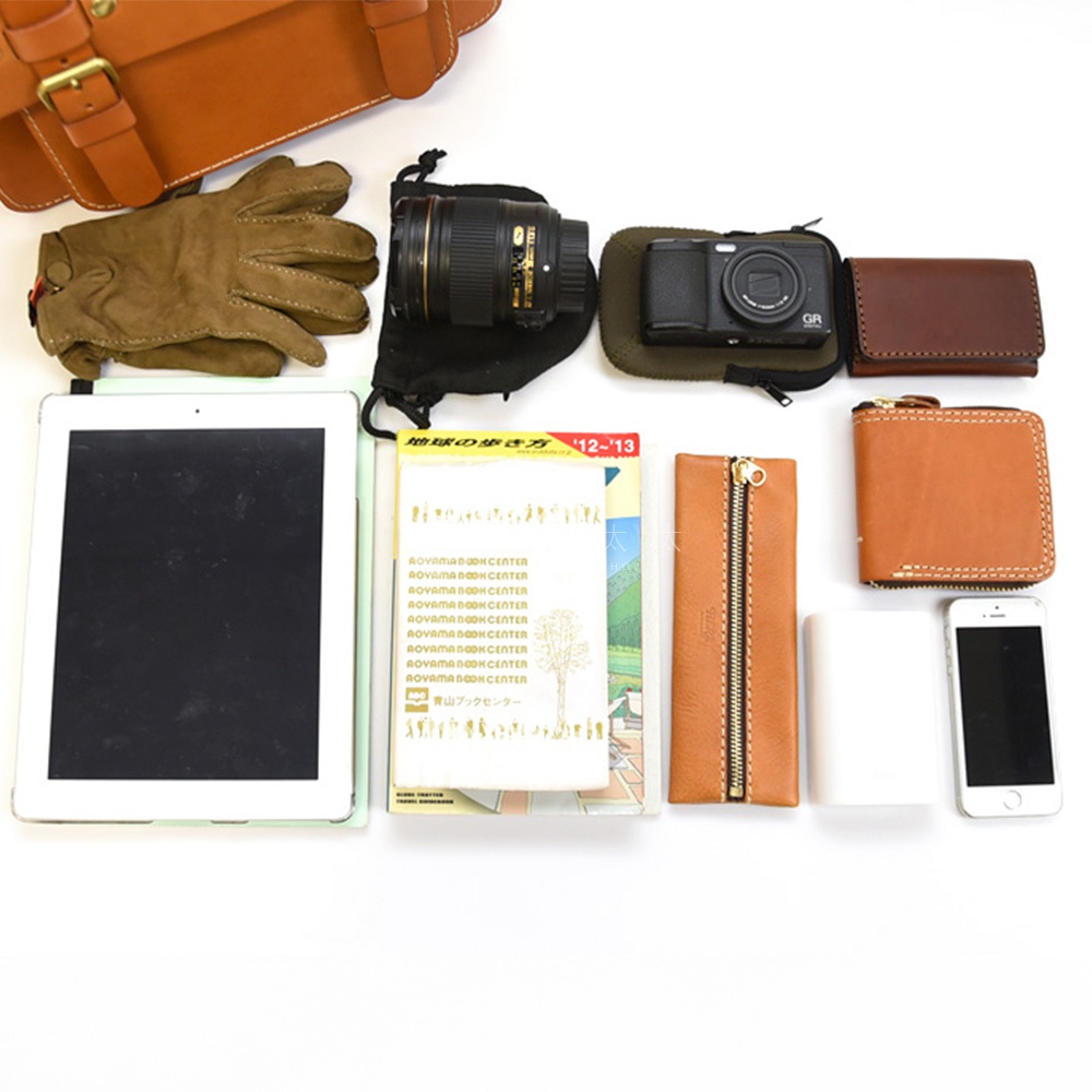皮革經典雙扣兩用單肩包，搭配棕色皮革手套、鏡頭、相機、平板電腦、書本、筆袋、錢包及手機。