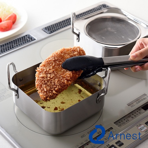 逸品物創不鏽鋼方型炸物鍋組，包含一個方形不鏽鋼炸鍋，鍋內有金黃色炸油，一塊裹滿麵包粉的炸物正由黑色夾子夾起，鍋的後方為另一組不鏽鋼炸鍋，鍋內放置濾油網。