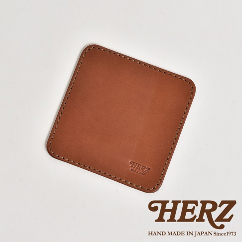 日本HERZ職人手作正方形皮革印章墊板，使用厚實的棕色Latigo皮革製成，表面呈現細緻的皮革紋理與邊緣縫線細節，右下角壓印品牌標誌，下方並附有HERZ品牌商標與產地說明文字。