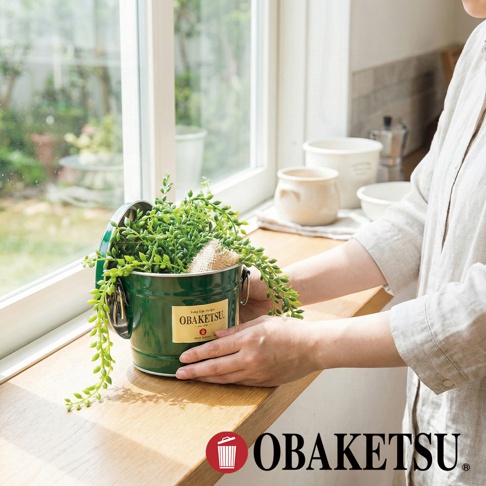 OBAKETSU 手工製綠色迷你桶，內有盆栽植物，放在木製窗台上，背景是窗戶和廚房。