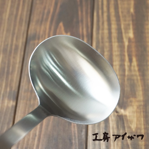 一個銀色不鏽鋼萬用湯勺，勺面寬大，手柄部分可見，背景為木紋桌面。