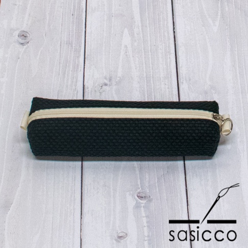 黑色三河木綿刺子織筆袋，帶有米白色拉鍊和金屬拉環，呈現簡約紡織紋理。
