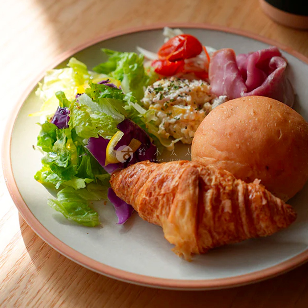 淺色陶瓷主菜盤，盤中盛有豐盛的早午餐，包括新鮮的綠葉沙拉、烤番茄、肉類、馬鈴薯沙拉、一個圓麵包和一個可頌。