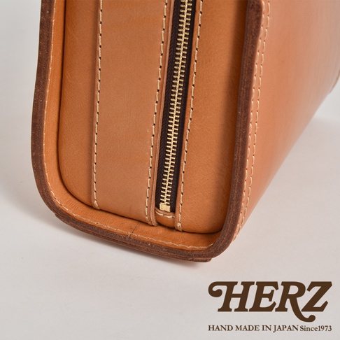 淺棕色皮革製作的方形單肩包，帶有金屬拉鍊和縫線細節，展現職人手作質感。