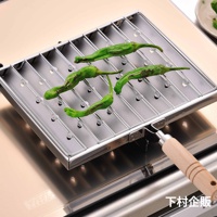 瓦斯爐專用炭烤風萬用燒烤盤，由不鏽鋼製成，設有條狀烤架，烤架上擺放著四根綠色辣椒，烤盤下方為金屬爐面。