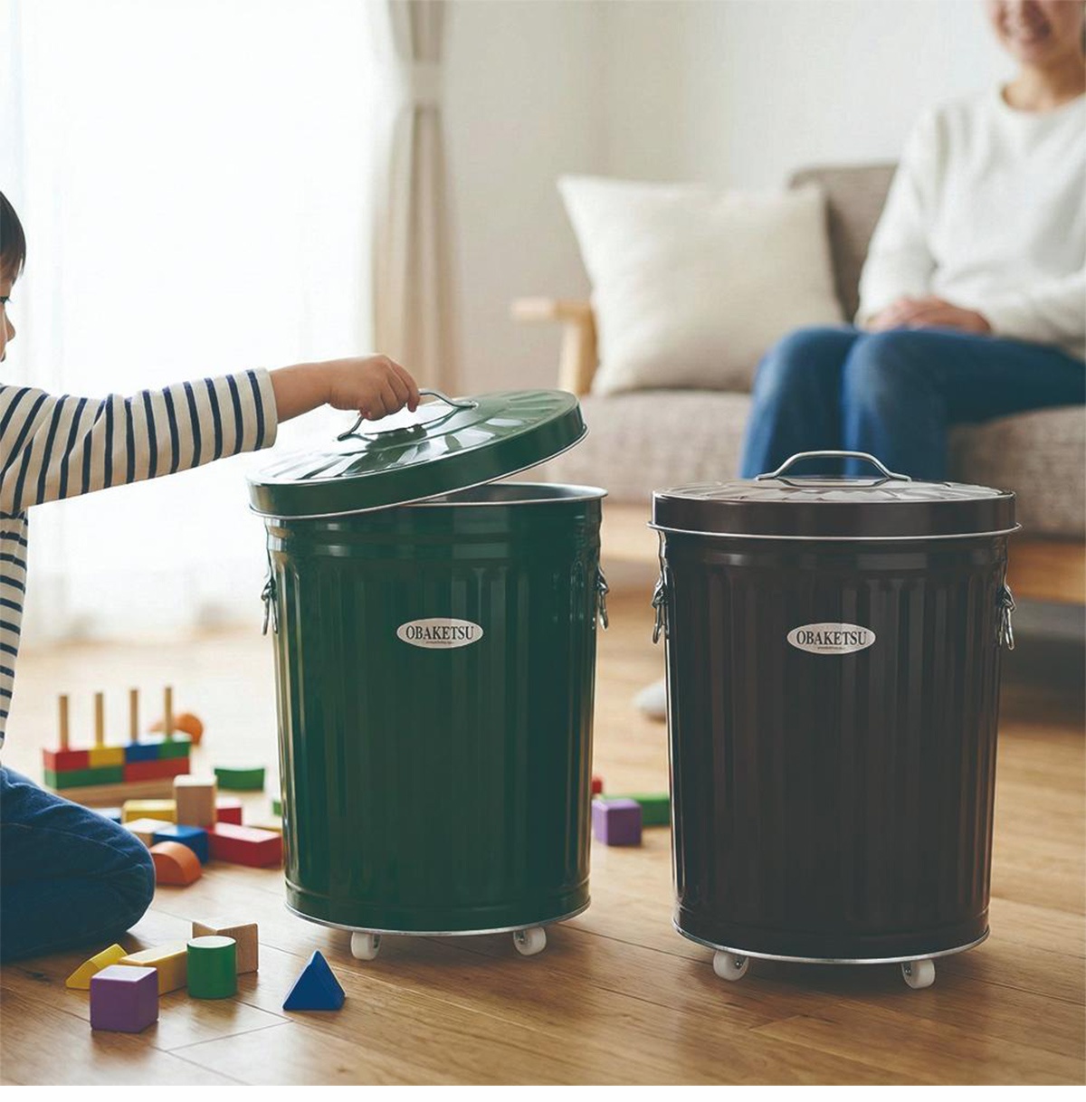 OBAKETSU 品牌綠色和棕色附輪垃圾桶，其中綠色垃圾桶的蓋子被一個小孩打開。
