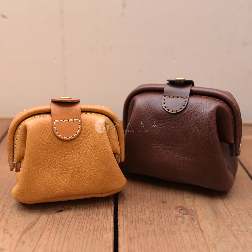 兩款職人手作皮革口金化妝包，一款為芥末黃色，另一款為深棕色。兩者皆為皮革材質，設計簡約，帶有金屬扣環，適合收納化妝品。